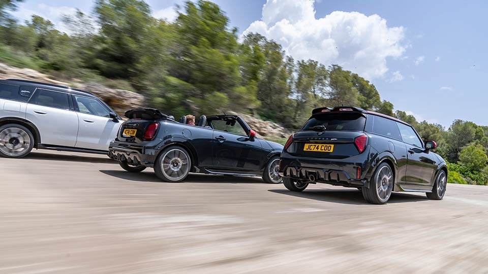 Three MINI models racing. A MINI Cooper, Countryman and Convertible captured from the side, speeding down an open road.